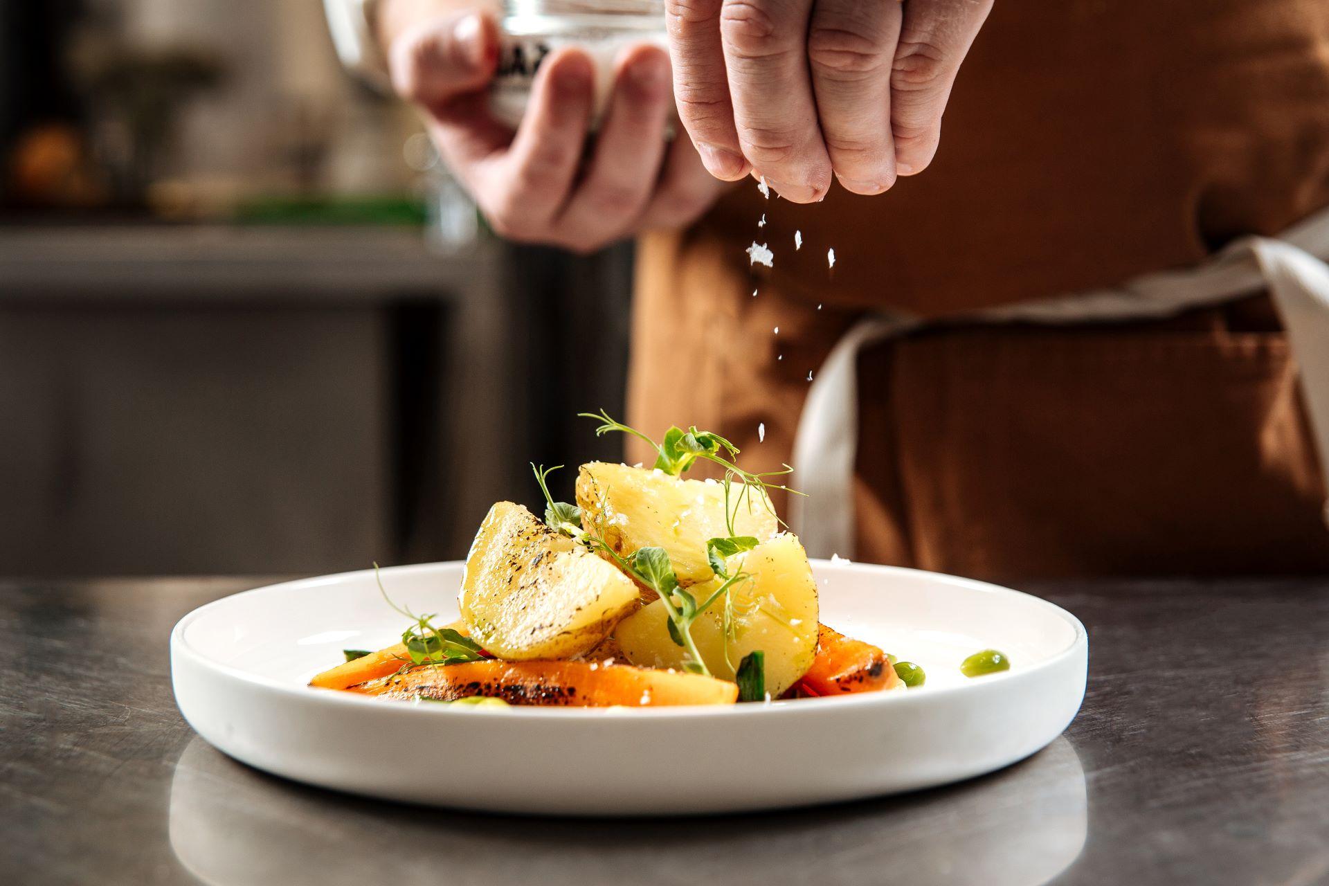 Die Hand des Küchenchefs bestreut das gekochte Gourmetgericht mit Salz